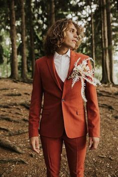 a man in an orange suit and flower boutonniere stands in the woods