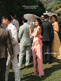 a woman in a pink dress holding an umbrella next to other people on the grass