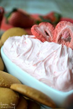 a bowl filled with whipped cream surrounded by cookies and strawberries on a tablecloth