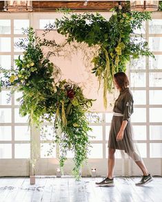 a woman is walking in front of a wall with plants hanging from it's sides