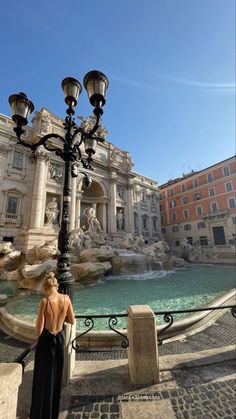 a woman standing next to a light pole near a fountain