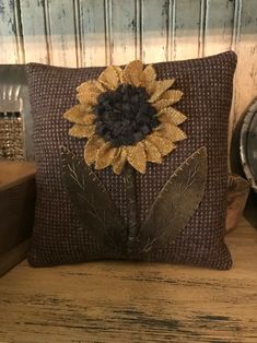 a decorative pillow with a sunflower on the front and leaves on the back, sitting on a wooden table