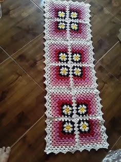 a crocheted table runner is on the floor next to a child's hand