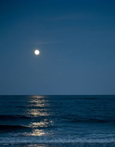 the moon is setting over the ocean with waves