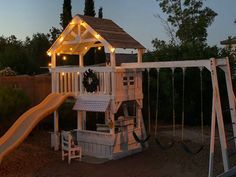 a wooden swing set with lights on it and a slide next to it in the evening