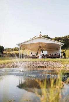 a gazebo on the side of a lake with people sitting at it and drinking water