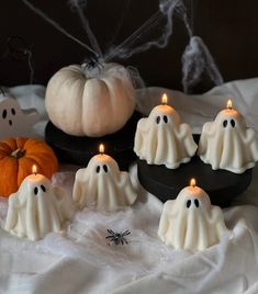 halloween candles with ghost faces and pumpkins in the background on a white cloth covered tablecloth