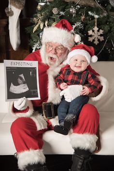 a baby sitting on santa claus's lap next to an older man holding a card