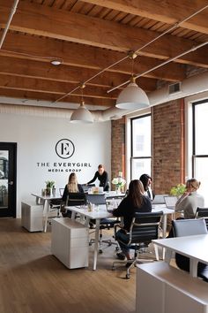 people sitting at desks in an office with large windows and exposed wood ceilinging