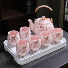 a pink tea set on a tray with six cups and a teapot in the middle