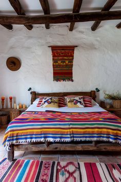 a bed with colorful blankets and pillows in a room next to a rug on the floor