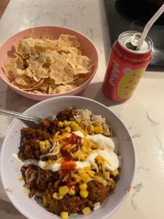 a bowl of chili, corn and nachos next to a can of soda