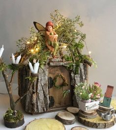 a fairy figurine sitting on top of a tree stump house surrounded by greenery