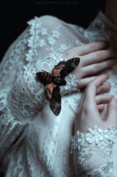 a woman in a white dress holding a butterfly on her arm and wearing lace gloves