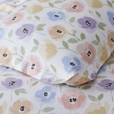 a close up of a bed with flowers on the sheets and pillow cases in pastel colors