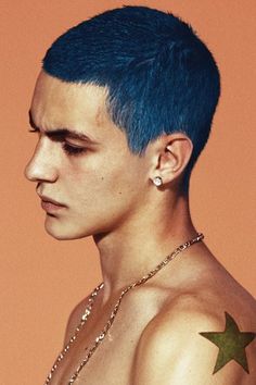 a young man with blue hair and piercings on his chest wearing a star necklace