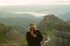 a man standing on top of a mountain next to a lush green valley filled with mountains