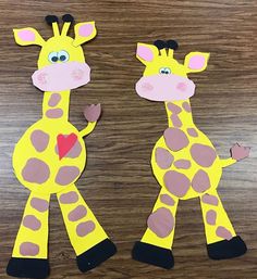 two giraffes made out of paper on a wooden table with one holding a heart