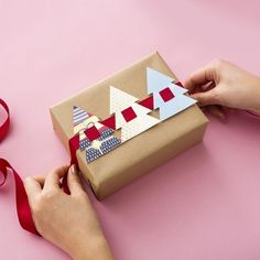 someone is wrapping up a gift on a pink surface with red ribbon and tape around it