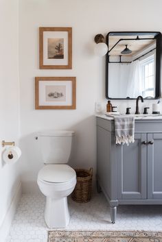 a white toilet sitting next to a sink in a bathroom under a mirror and framed pictures on the wall