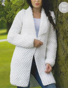 a woman leaning against a tree wearing a white crochet coat