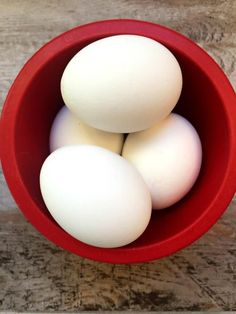 three eggs in a red bowl on a wooden table