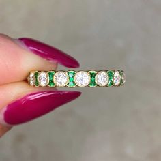 a woman's hand holding a ring with diamonds and emeralds on the side