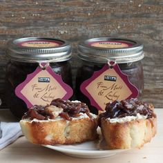 three jars of jam sit on a table next to a plate with two muffins