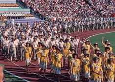 a large group of people in uniforms marching on a track with an audience behind them