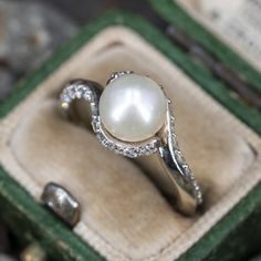 This beautiful ring features a by-pass design and is centered with one (1), post set, cultured saltwater pearl. The top half of the shank is accented with twenty- four (24), shared prong set, round brilliant cut diamonds. The ring measures 9.0mm at the top, rises 8.3mm above the finger, tapering to 2.2mm wide and 2.2mm thick at the base of the shank. This ring is currently a size 4.5. Anniversary Jewelry With Rose Cut Diamonds And Pearls, Elegant Bypass Ring With Center Stone For Wedding, Elegant Pearl Ring With Rose Cut Diamonds For Anniversary, Elegant Wedding Bypass Ring With Diamond Accents, Elegant Wedding Bypass Ring, Elegant Silver Pearl Ring With Rose Cut Diamonds, Elegant Sterling Silver Bypass Ring For Wedding, Elegant Pearl Ring With Rose Cut Diamonds, Elegant Wedding Bypass Ring With Center Stone