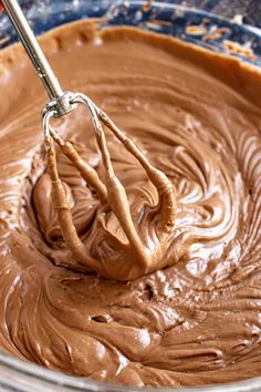 a mixing bowl filled with chocolate frosting and a whisk in the middle