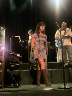 a woman standing on a stage in front of microphones and music instruments with other musicians behind her