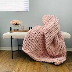 a pink knitted blanket sitting on top of a wooden floor next to a white bench