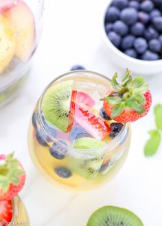 a glass filled with fruit on top of a table next to bowls of berries and kiwis