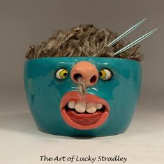 a blue bowl with a face and two needles sticking out of it's mouth