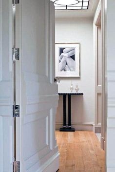 an open door leading to a room with white walls and wood floors, along with a painting on the wall