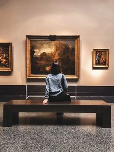 a woman sitting on a bench in front of paintings