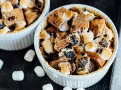 two bowls filled with dessert and marshmallows on top of a black table