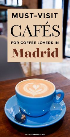 a cup of cappuccino sitting on top of a blue saucer next to a sign that says must - visit cafes for coffee lovers in madrid