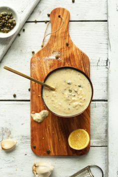 a wooden cutting board topped with a bowl filled with soup next to an orange slice