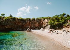 people are sitting on the beach and swimming in the clear blue water near some cliffs