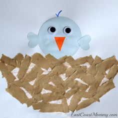 a paper plate bird sitting on top of a pile of cut up pieces of cardboard