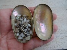 a person is holding an open shell with beads and a cross on it in the palm of their hand