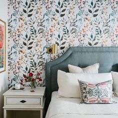 a bedroom with floral wallpaper and blue headboard, white bedding, and two nightstands