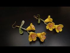 three yellow crocheted orchids are hanging from hooks on a black surface,