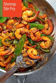 a pan filled with shrimp and peppers on top of a table next to a wooden spoon