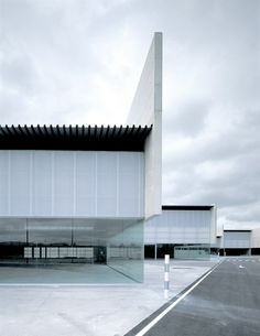 an empty parking lot in front of a large building with glass walls and doors on the sides