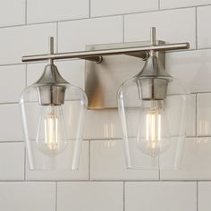 two light fixtures mounted on a white tiled wall in a bathroom with glass shades over the bulbs