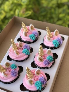 cupcakes with pink frosting and unicorn decorations in a box on a table