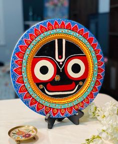 a colorful plate with a face on it sitting on a table next to a flower